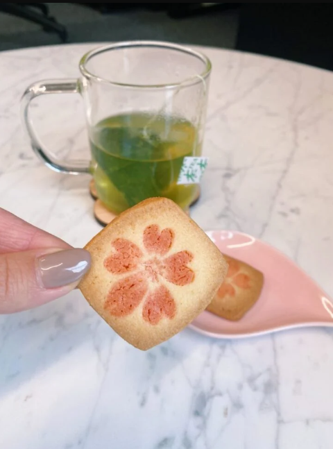 A female subscriber holding a floral cookie in front of green tea from her Bokksu delivery.