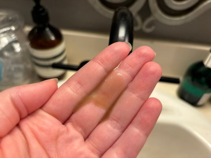 brown liquid skincare serum in a hand over a sink